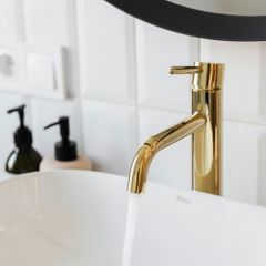 Detail shot of a luxury bathroom renovation featuring a sleek white vessel sink and a polished gold contemporary faucet.