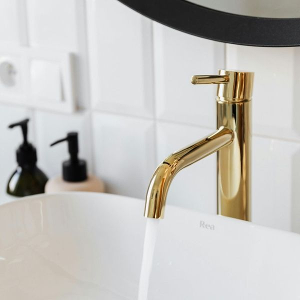 Detail shot of a luxury bathroom renovation featuring a sleek white vessel sink and a polished gold contemporary faucet.