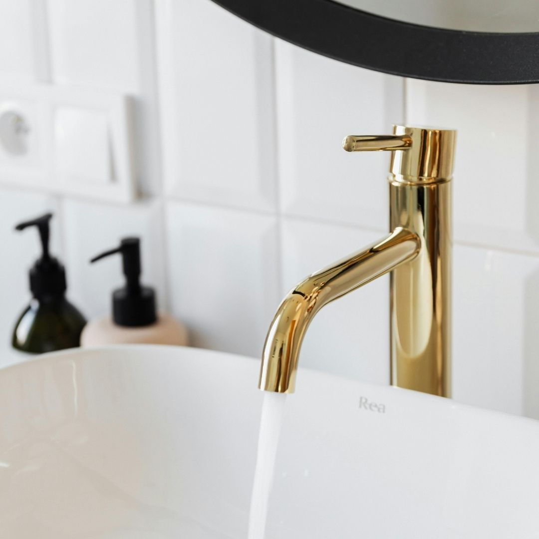 Detail shot of a luxury bathroom renovation featuring a sleek white vessel sink and a polished gold contemporary faucet.