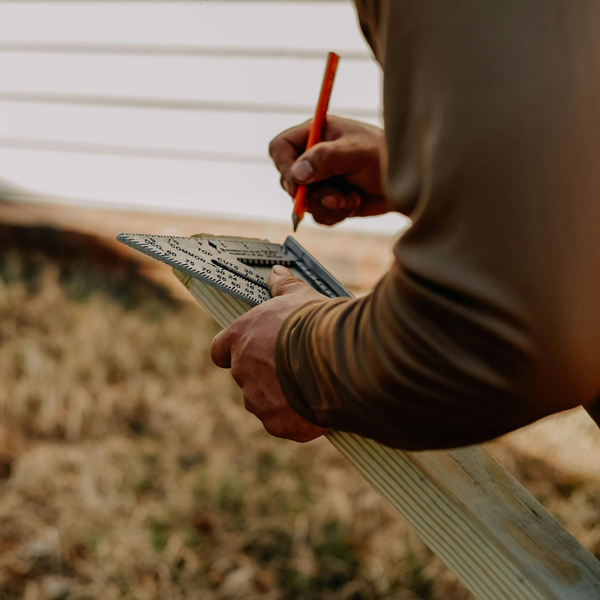 A craftsman using a speed square and pencil to mark accurate angles on a piece of lumber for a custom construction project