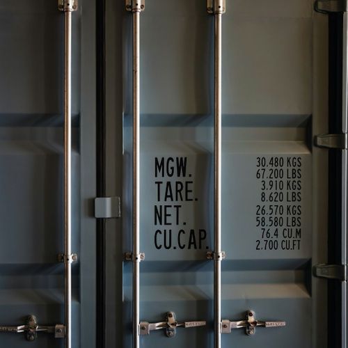 Close-up of a cargo shipping container door showing the technical specifications (weight, tare, capacity) stenciling, locking bars, and handles.