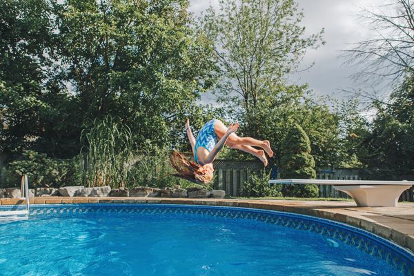 young girl jumping into backyard swimming pool jumping into swimming pool