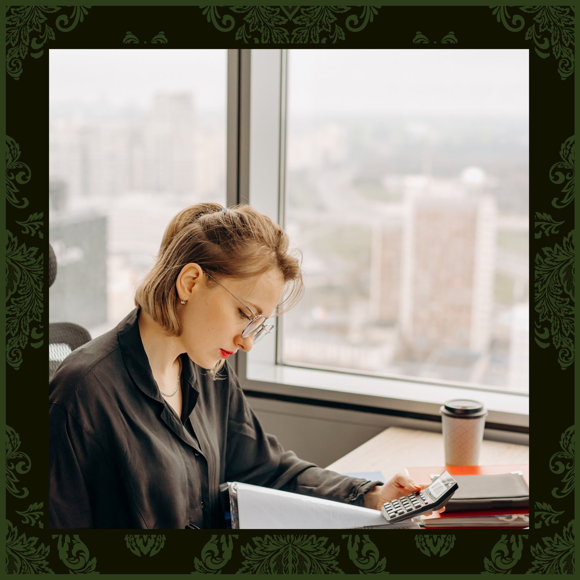 A professional woman in a black blouse and glasses working at a desk with a calculator and files, positioned in front of a large window with a city view.