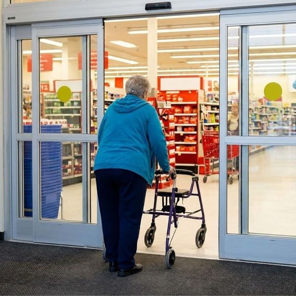 A person using a walker easily enters a retail store as the automatic sliding glass doors open.