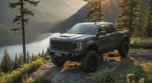 A gray pickup truck with off-road bumpers and fender flares parked on a rocky overlook, with a sunlit mountain lake and evergreen forest in the background. A gray pickup truck with off-road bumpers and fender flares parked on a rocky overlook, with a sunlit mountain lake and evergreen forest in the background.