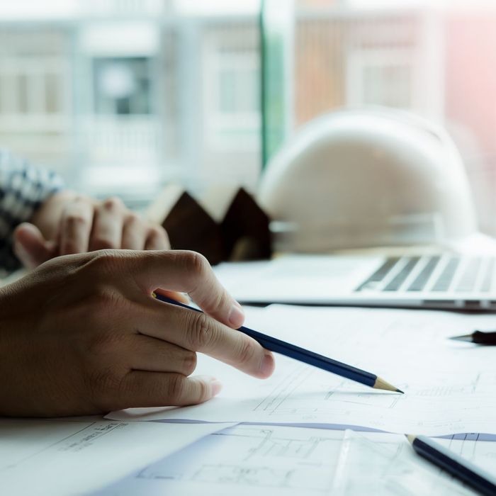 pointing at blueprints with pencil, laptop and hard hat in background
