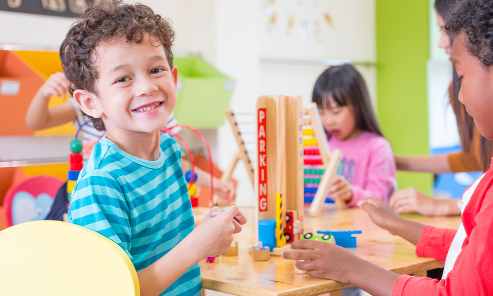 Image of a preschool aged boy smiling while learning with other children