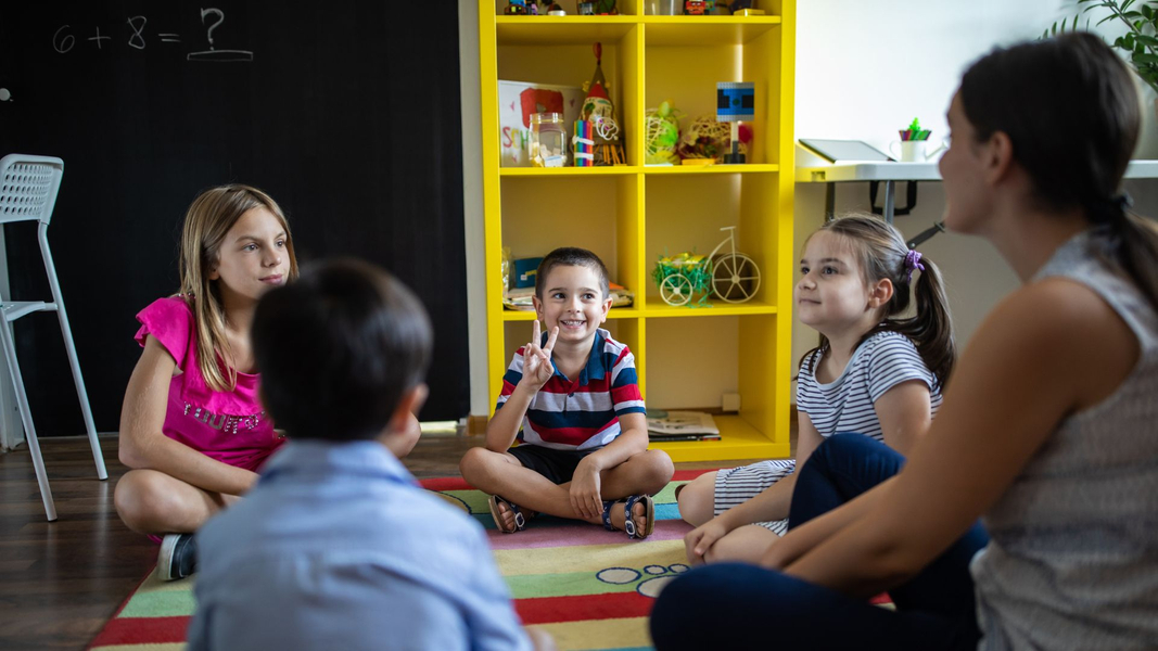 kids sitting on a mat with a teacher. 