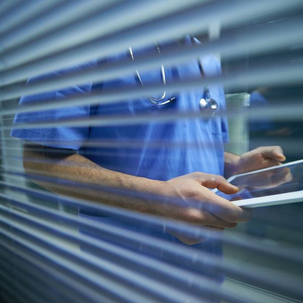 View through window blinds of a doctor or nurse looking at a tablet