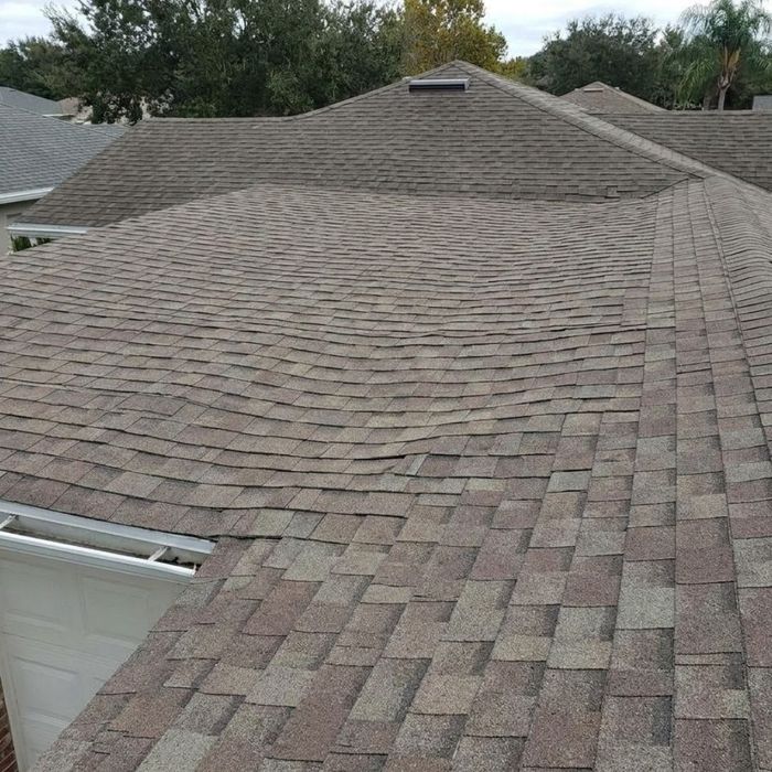 A wide shot of a residential home against a blue sky, showing a slight, visible sagging in the roof line.