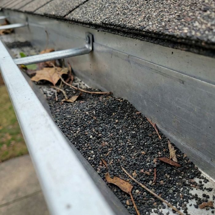 A rain gutter filled with black asphalt shingle granules.