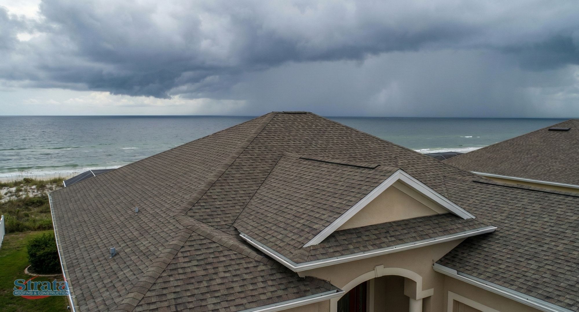 An aerial view of a residential roof on the coast with storm clouds approaching over the ocean.