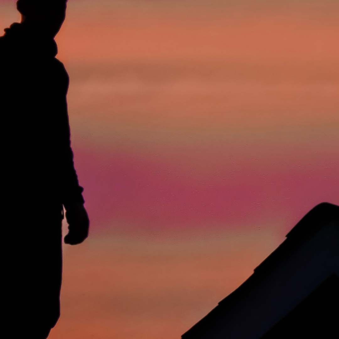 A silhouette of a roofing contractor on a roof at sunset.