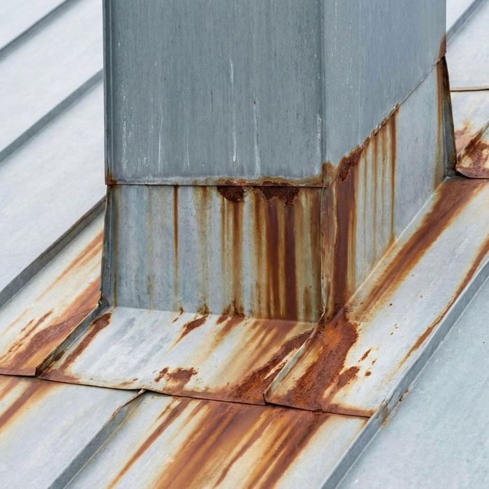 Rust corrosion on metal flashing around a roof chimney.