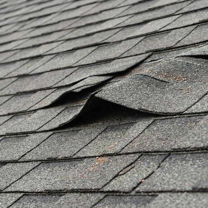 Close-up of asphalt roof shingles lifted and damaged by high winds.