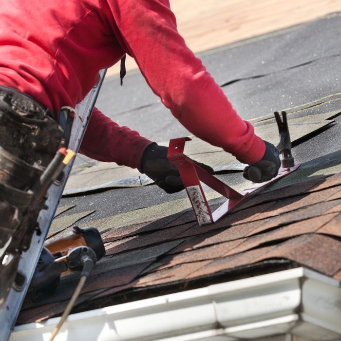 A person installing a shingle with a hammer