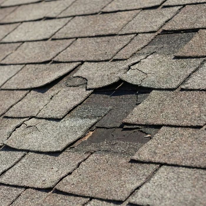 Close-up of damaged asphalt shingles that are cracked and missing pieces.