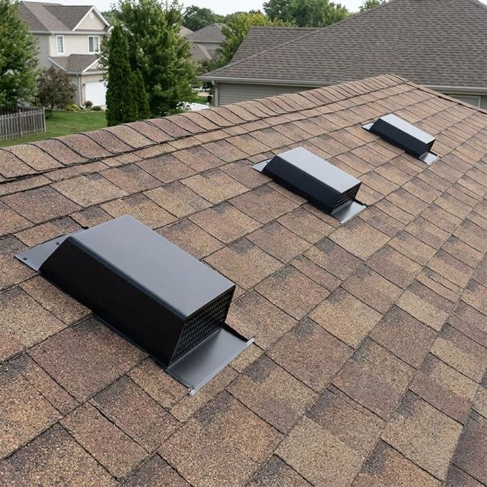 A medium shot of several dark gray roof vents installed neatly along the ridge of a residential home's roof.