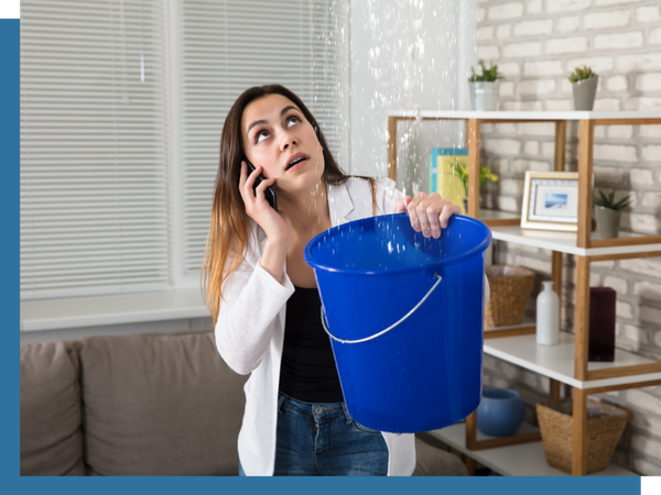 woman on phone holding bucket under ceiling leak