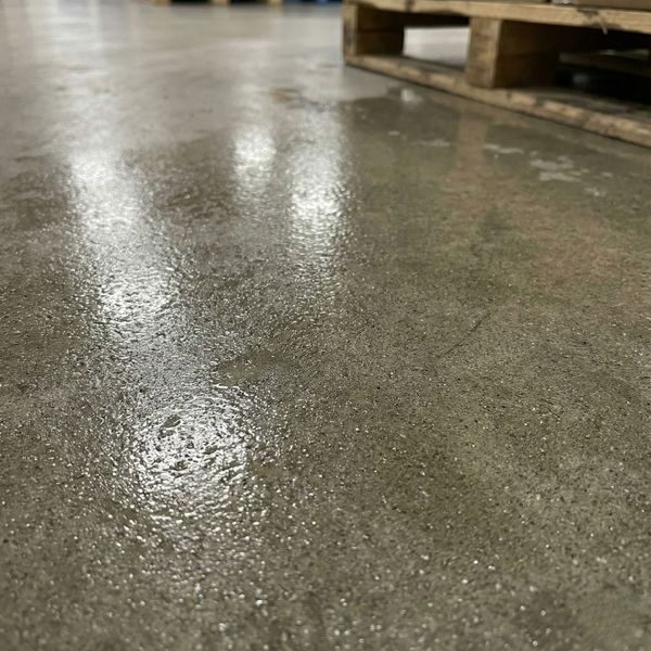 Close-up detail of moisture beading on a concrete warehouse floor, illustrating sweating slab syndrome.