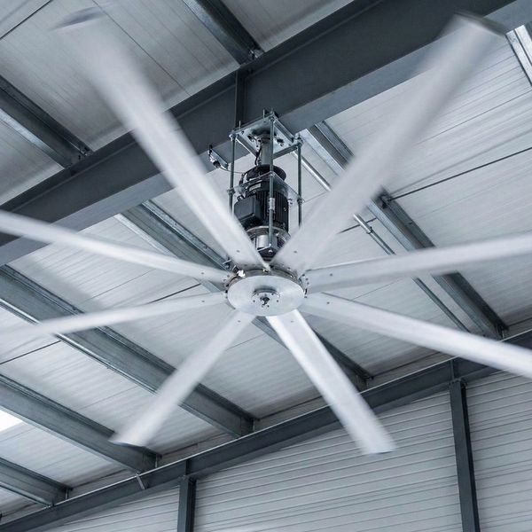 Low angle view of a large industrial HVLS fan spinning on a warehouse ceiling to improve airflow.