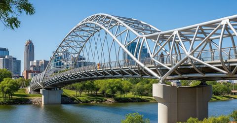 A complete view of a newly built pedestrian bridge with a geometric steel design spanning a river.