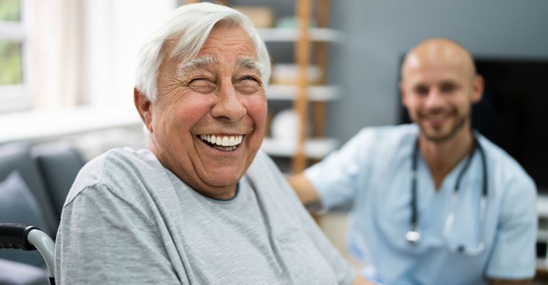 A very happy older man smiling while speaking to a nurse