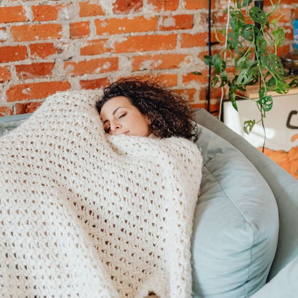 woman curled up with a blanket on a blue couch