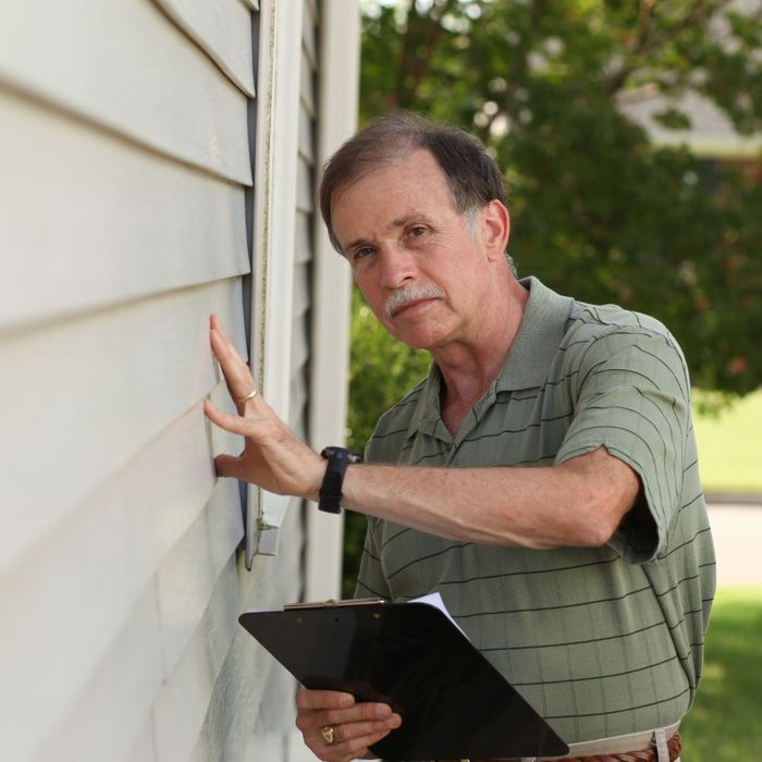 person holding clipboard while touching outside house siding