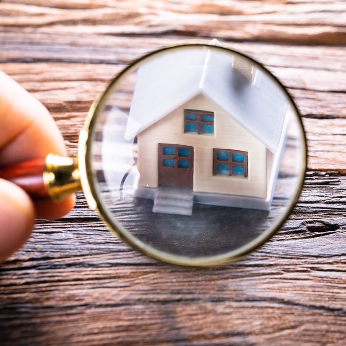 person looking at model toy home through magnifying glass