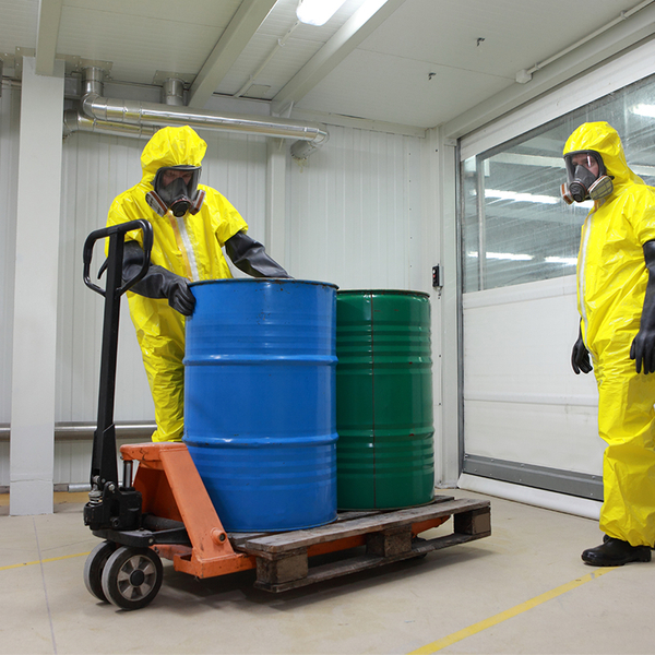 Two workers in HazMat suits loading barrels on a pallet