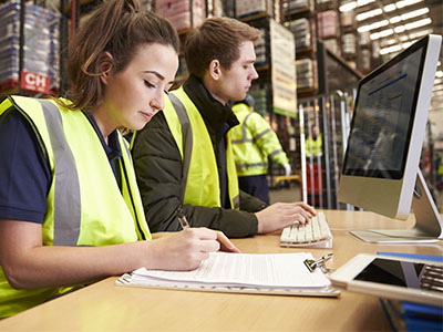 Two warehouse employees working at a desk with a computer