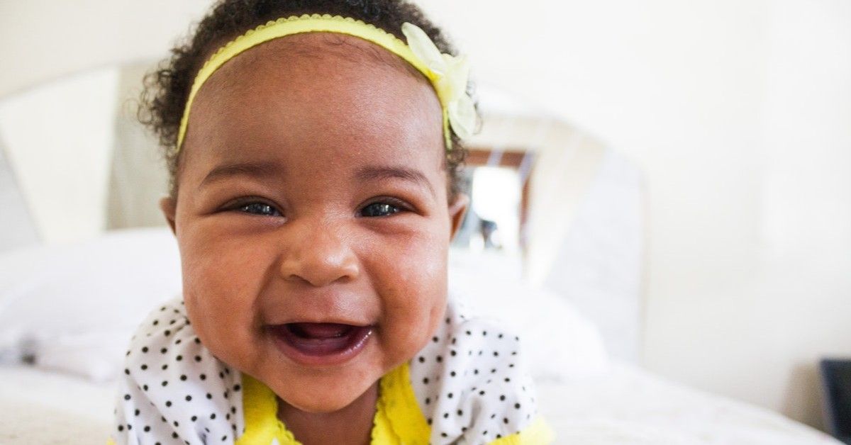 baby girl sitting on bed happily laughing