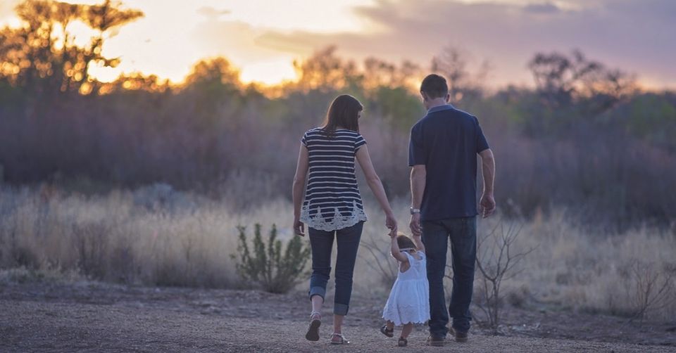 couple and their child walking in a field with sun setting 