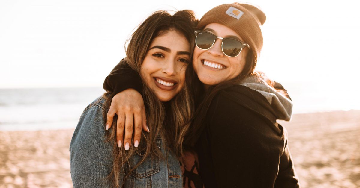 women embracing and smiling on the beach on a cool day