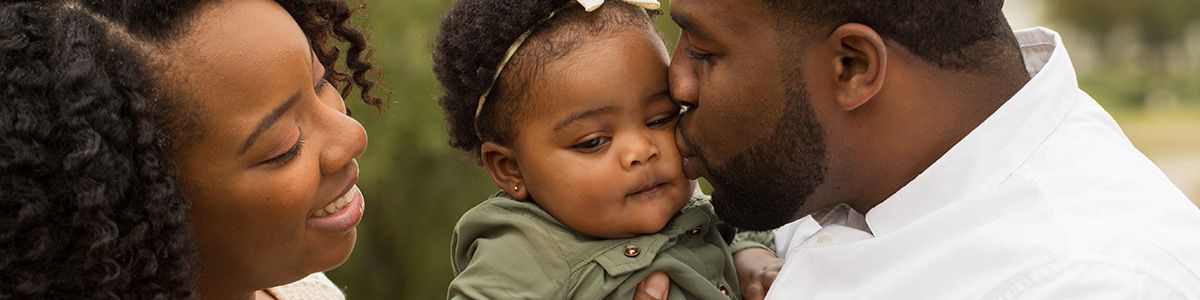 couple holding baby girl - dad giver her a kiss