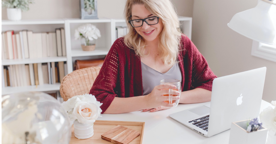 Woman smiling holding tea at desk with laptop