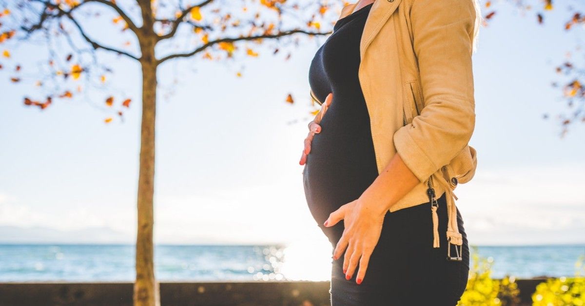 pregnant woman in black dress in front of ocean backdrop