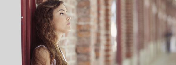 woman leaning against doorway of a bricked building hallway