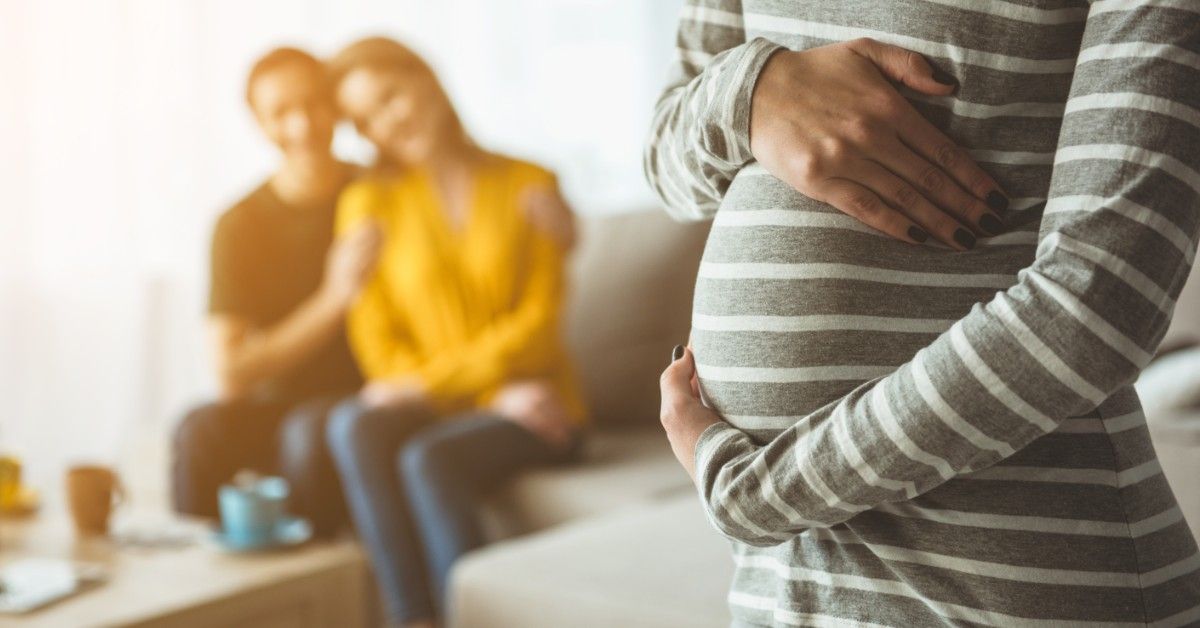 woman holding pregnant belly with couple sitting in background