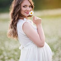 pregnant woman in white dress holding flower to her nose