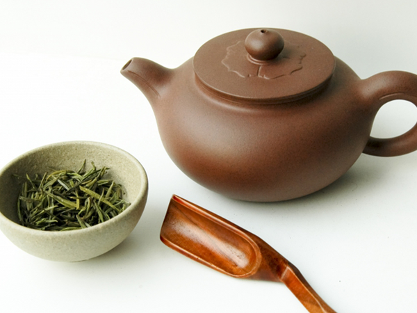 Brown teapot with wooden spoon and small bowl of tea leaves