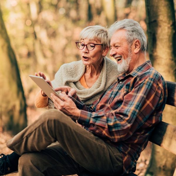 elderly man and woman smiling at a tablet in the park