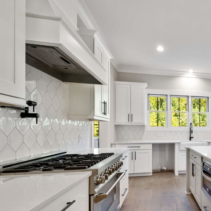  A modern kitchen with a large island, white granite countertops, sleek matte white cabinets, and stainless steel appliances.