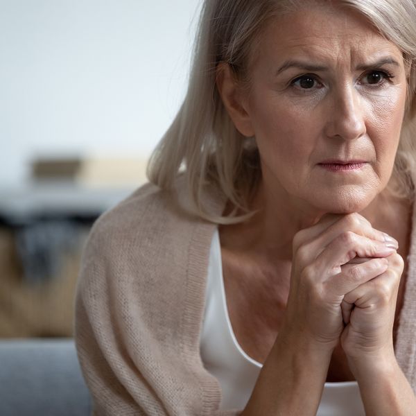  Older woman looking concerned or worried with her hands clutched below her face.