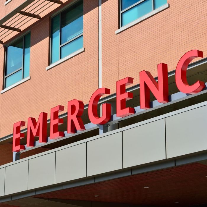 The exterior of a hospital building with a large red sign above the entrance that reads "EMERGENCY."