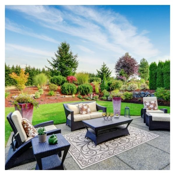 Outdoor patio with furniture, garden, and trees in background