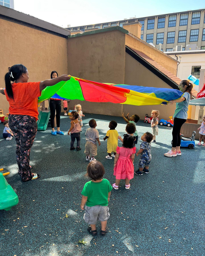 Child care staff and children playing a parachute game outside