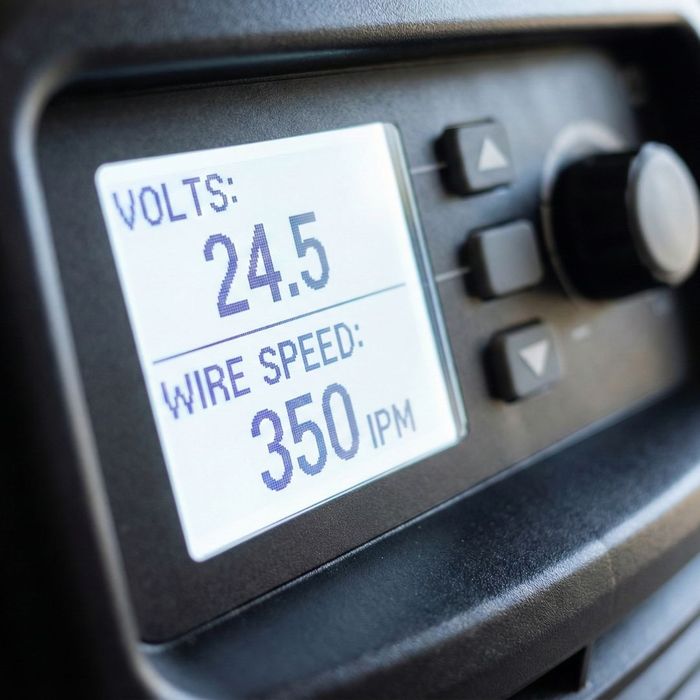 An extreme close-up of a digital LCD screen on a welding machine displaying precise voltage and wire speed settings.