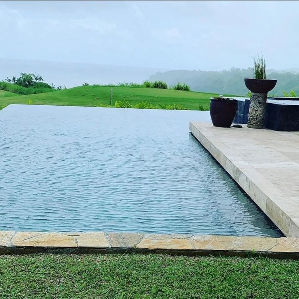 A calm infinity edge pool overlooking a rolling green landscape and the ocean on a cloudy day in Kauai. A calm infinity edge pool overlooking a rolling green landscape and the ocean on a cloudy day in Kauai.